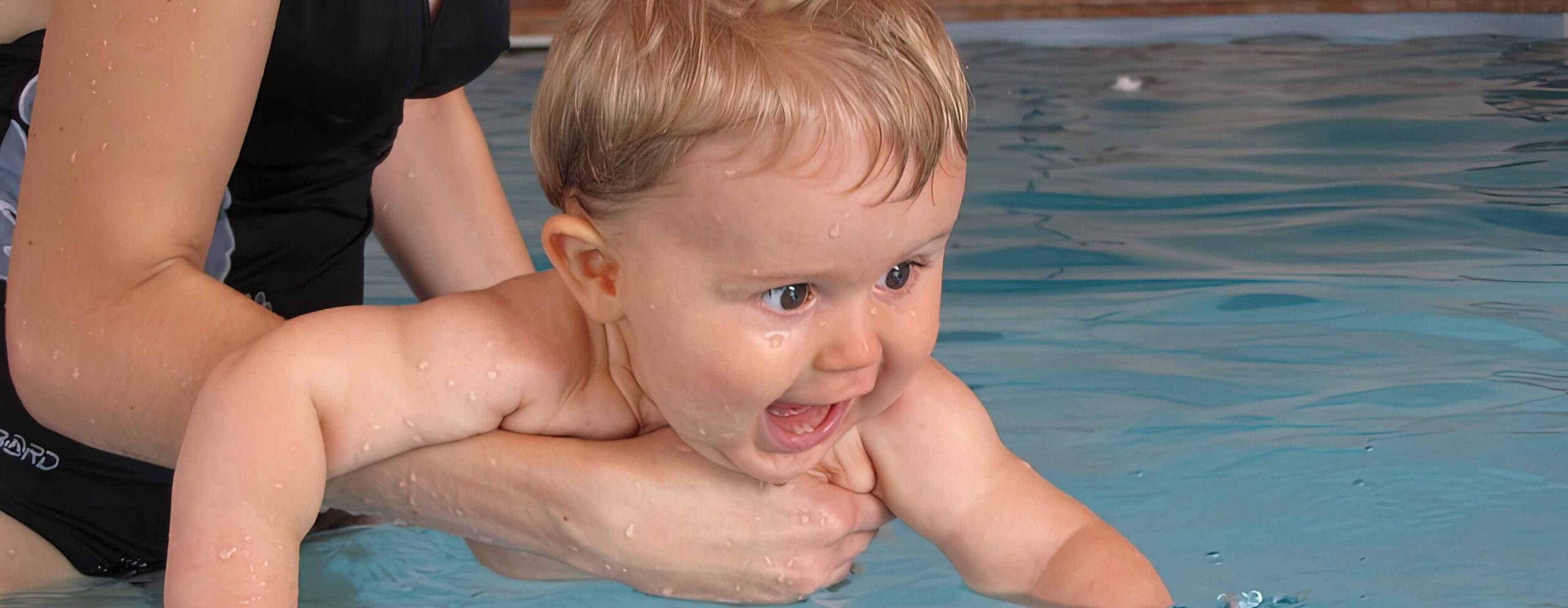 a baby in a swimming pool playing with a woman.